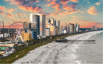 SkyWheel Myrtle Beach, the Myrtle Beach Pier, and many people enjoying the ocean in the early evening.