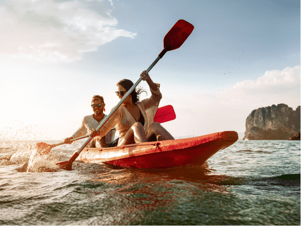 A couple kayaking along the ocean’s open waters in a red kayak on a bright afternoon.  