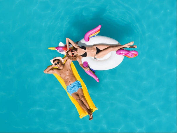 A man relaxing on a yellow pool float next to a woman relaxing on a unicorn pool float on top of stunning turquoise waters.