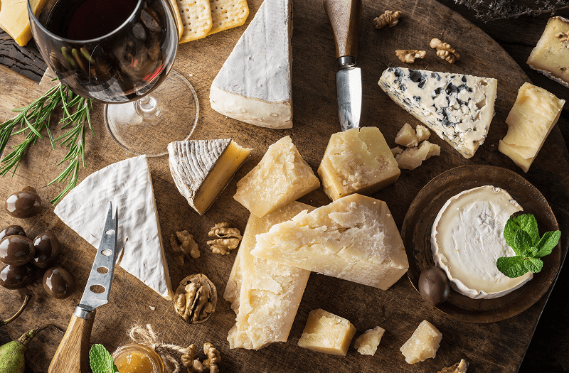 A wooden table topped with assorted cheeses and a glass of red wine.