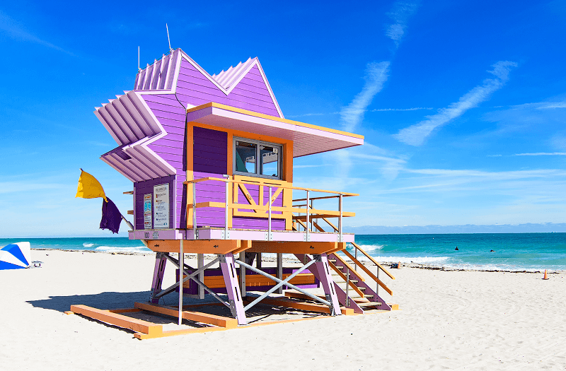 Unique purple and yellow Art Deco-style lifeguard tower along Miami Beach on a clear day.