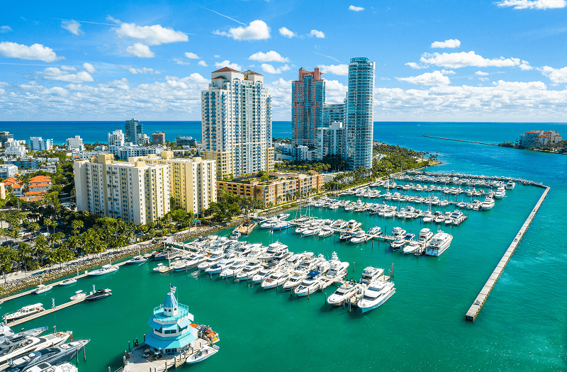 Aerial view of the Miami Beach Marina with many white boats docked next to tall high-rise buildings.