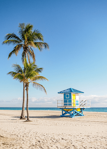 A vibrant yellow and blue lifeguard tower on the shores of Hollywood Beach near Miami on a clear day.