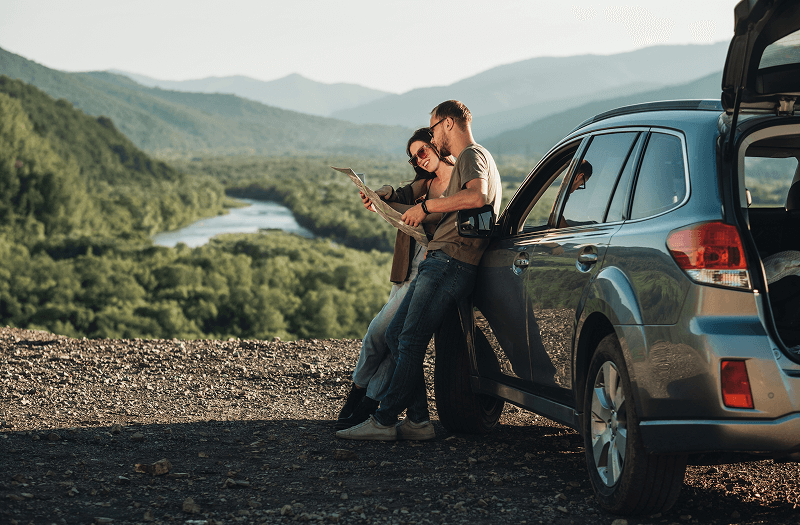 A man and woman leaning against an SUV in the mountains while they look at a map.