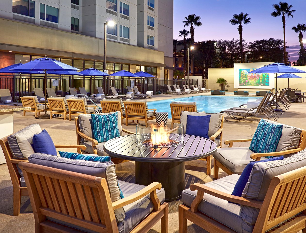 A sunset view of the pool area of the Cambria Hotel & Suites Anaheim Resort at a firepit table