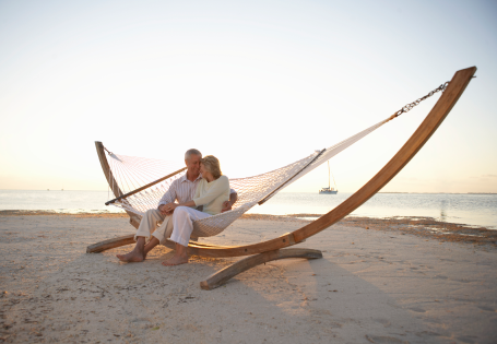 An older couple sitting in a hommock on a beach near sunset