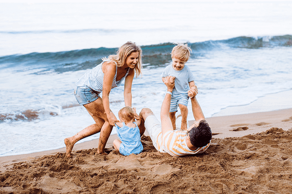 A family of four: mom, dad and two children enjoying the beach in the sand