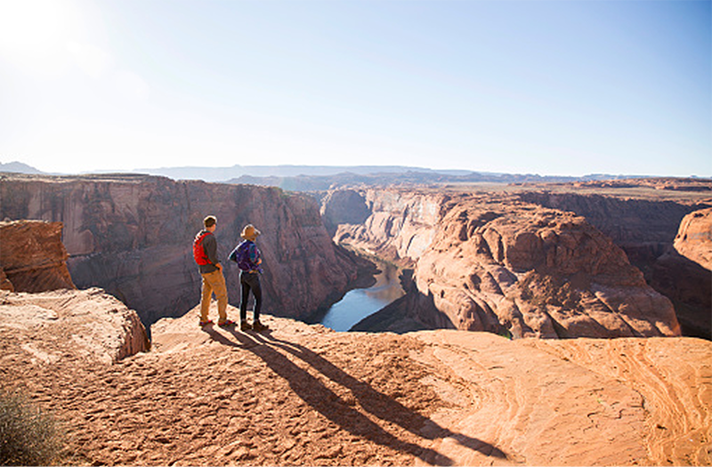 Two people stand on a cliff, gazing out over the vast canyon at Horseshoe Bend in the Glen Canyon National Recreation Area.