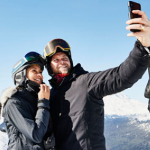 A couple taking a selfie in the mountains while doing snow sports.