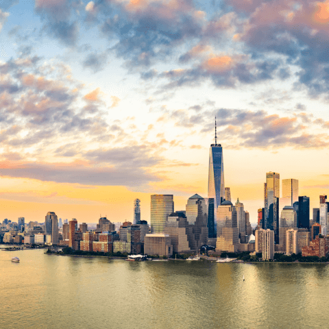 New York City skyline silhouetted against a vibrant sunset, with warm hues of orange and pink lighting up the sky.  