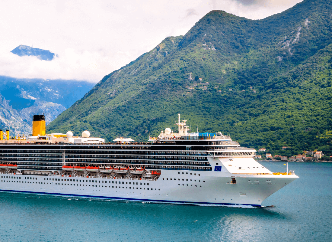 A large cruise ship sailing in the water in front of lush green mountains