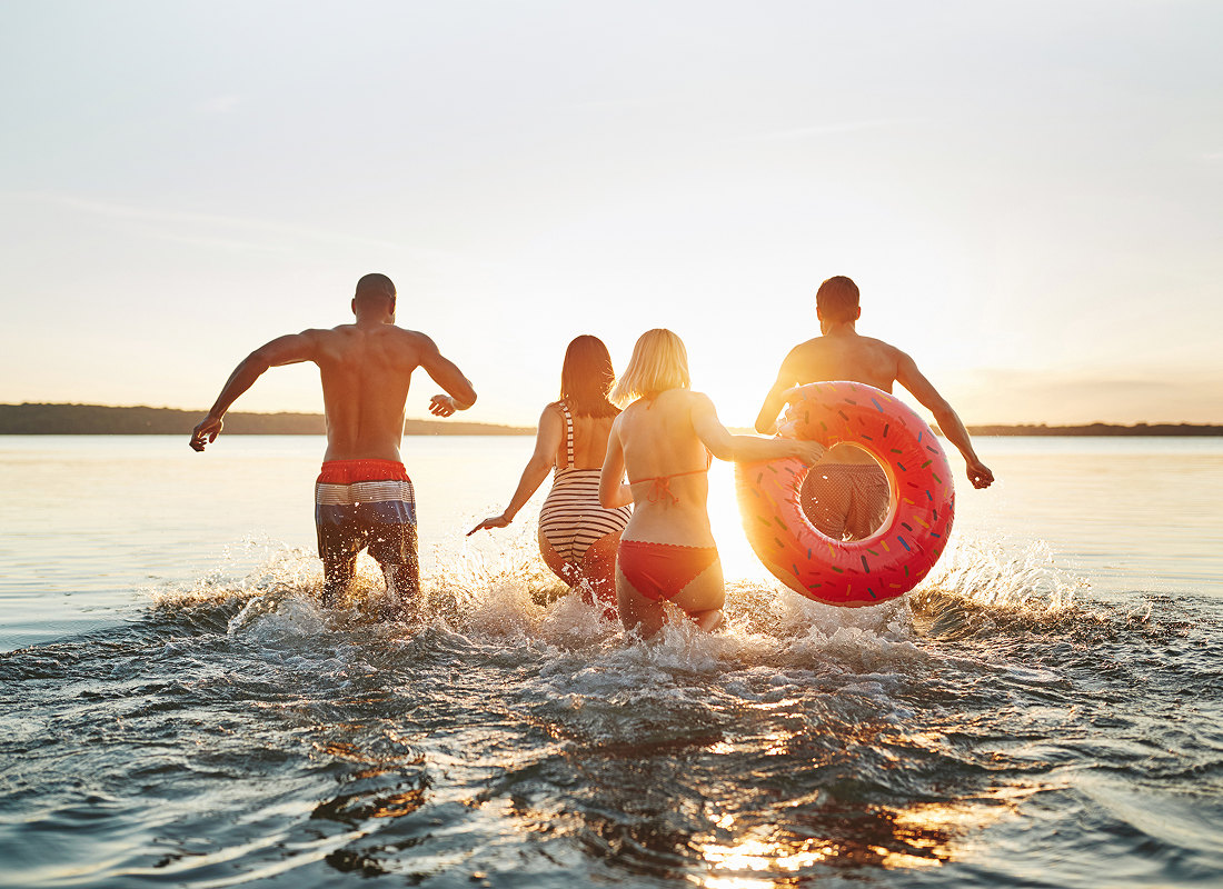 A group of four runs playfully in the water, with one person carrying a bright life ring.  