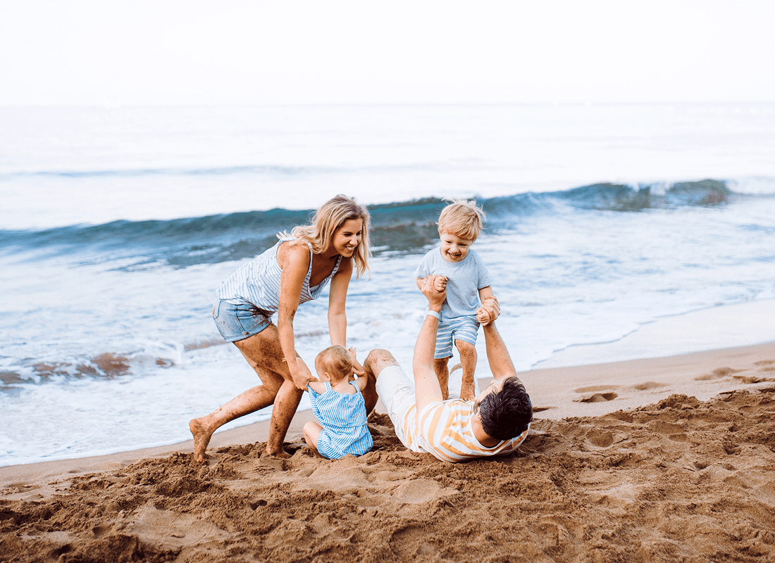 A cheerful family on the beach, engaging in playful activities with their children, surrounded by sand and waves.