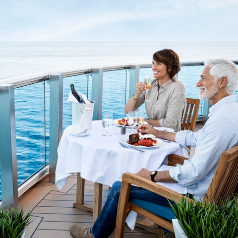 A couple enjoying a meal at the balcony of a cruise ship.