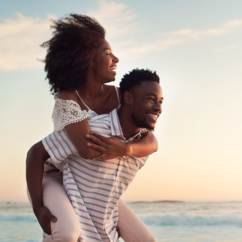 A man giving a woman a piggyback ride by the beach.