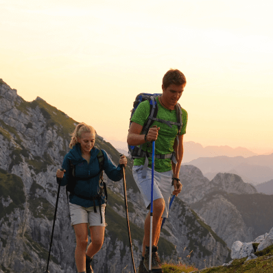 Two people hiking with walking sticks as the sun sets behind the mountains.