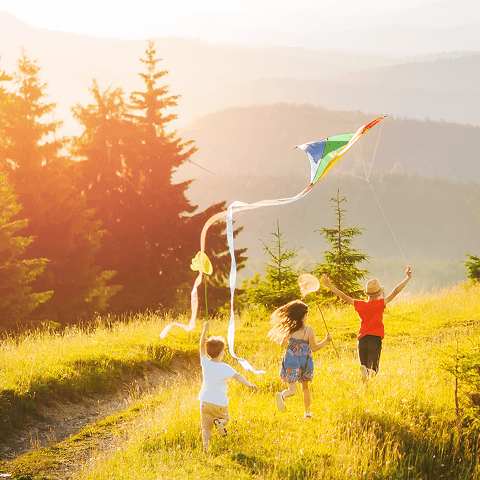 Three young kids running through a field with kites as the sun begins to set. 