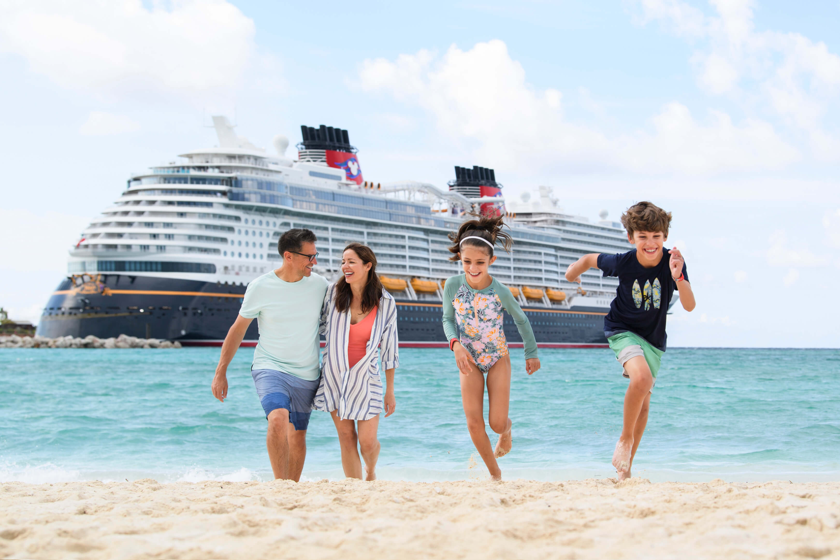 A family of four enjoying the beach with a Disney cruise liner in the distance.