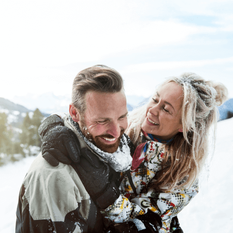 Smiling couple hugging outdoors in a snowy winter mountain setting.