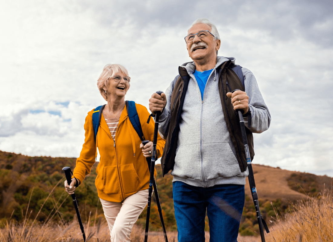 Happy senior couple hiking outdoors using trekking poles on a scenic trail.