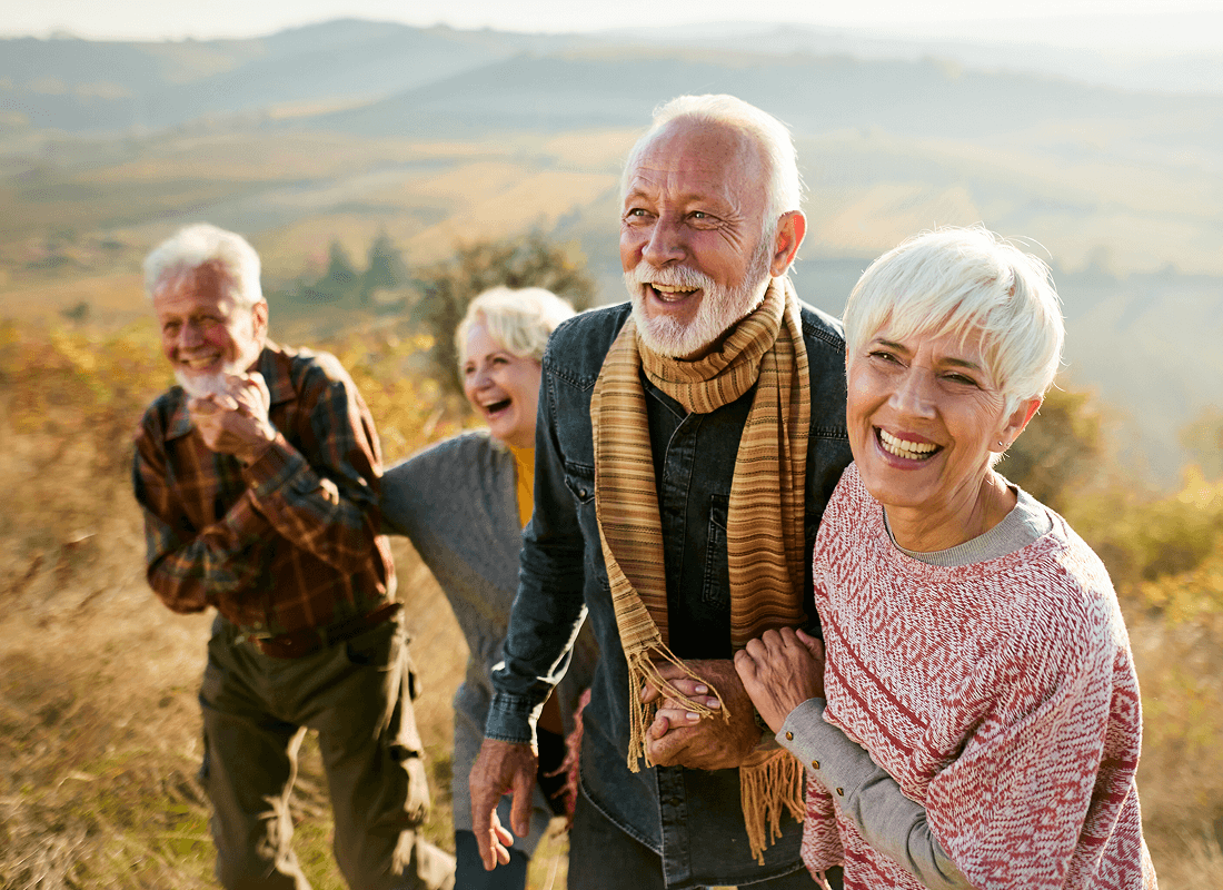 Two smiling older couples enjoying a walk along a grassy hill.