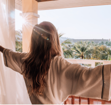 A woman in a bathrobe standing on a hotel balcony enjoying the morning sun
