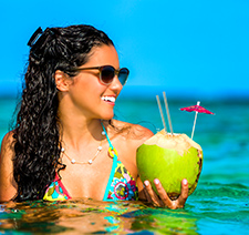 A woman with a tropical drink in a coconut standing in a pool