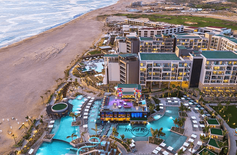 Aerial view of the colorful and expansive Hard Rock Hotel Los Cabos beside an empty shoreline.
