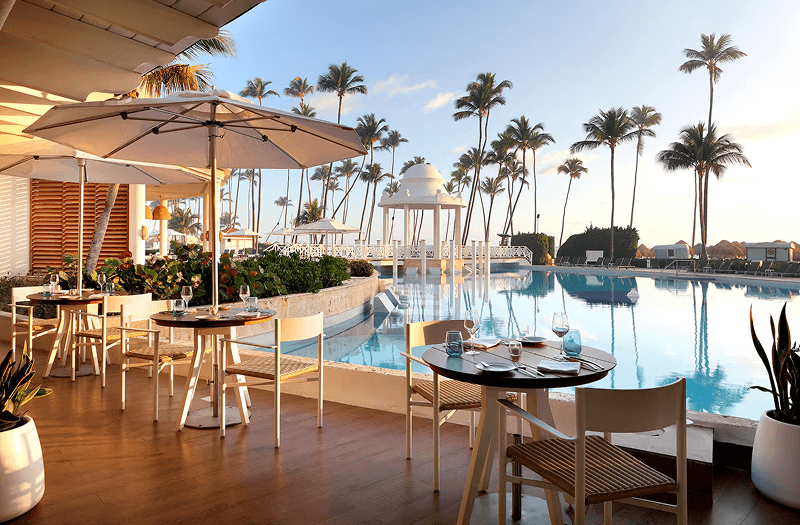 Tables and chairs overlooking the pool and wooden deck on a clear day at Paradisus Palma Real Golf & Spa Resort in Punta Cana.