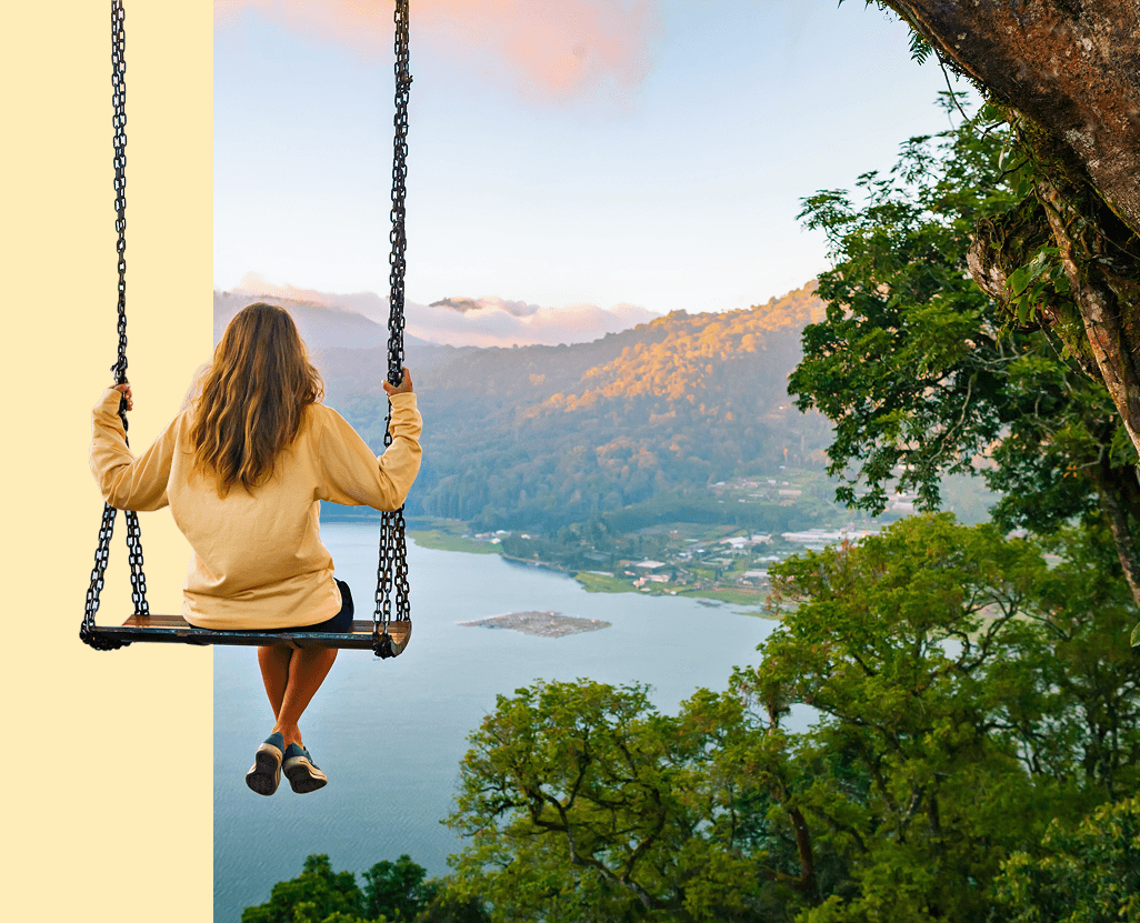 A girl swinging on a swing while overlooking a lake and rolling hills.