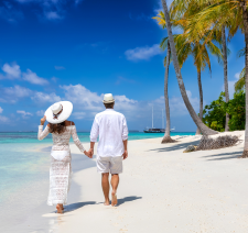 A couple in hats holding hands and walking on the beach