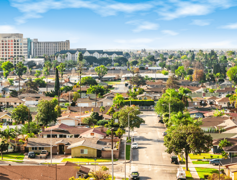 Sunny aerial view looking down a suburban street in Anaheim, California toward large resort buildings under a blue sky.