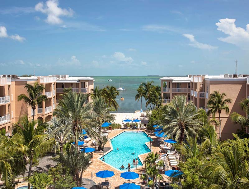 A bird's-eye view of the resort buildings and lushly-landscaped pool area, with the ocean visible in the background.