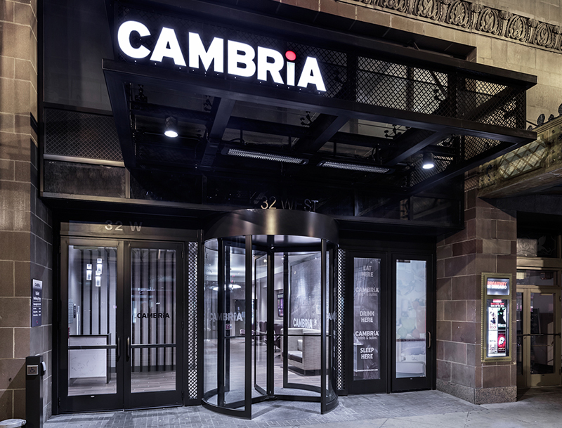 The Cambria Chicago Hotel entrance featuring a black industrial awning with illuminated signage and a revolving glass door.