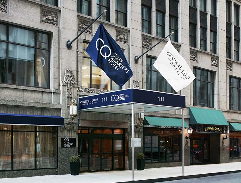 A street view of the hotel's facade featuring large windows and a welcoming entrance adorned with flags.