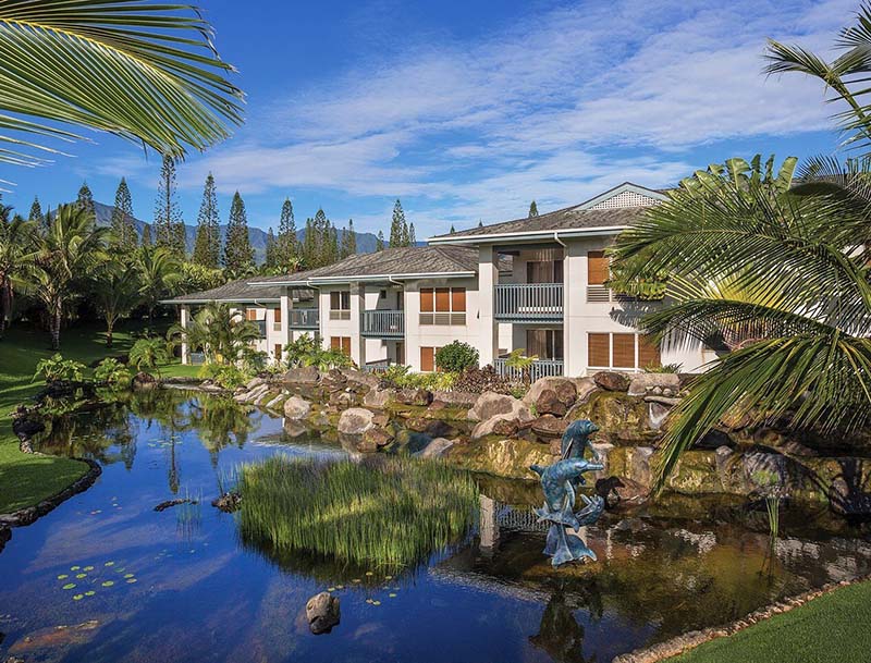 A resort nestled among lush vegetation with a large water feature in front of the building.