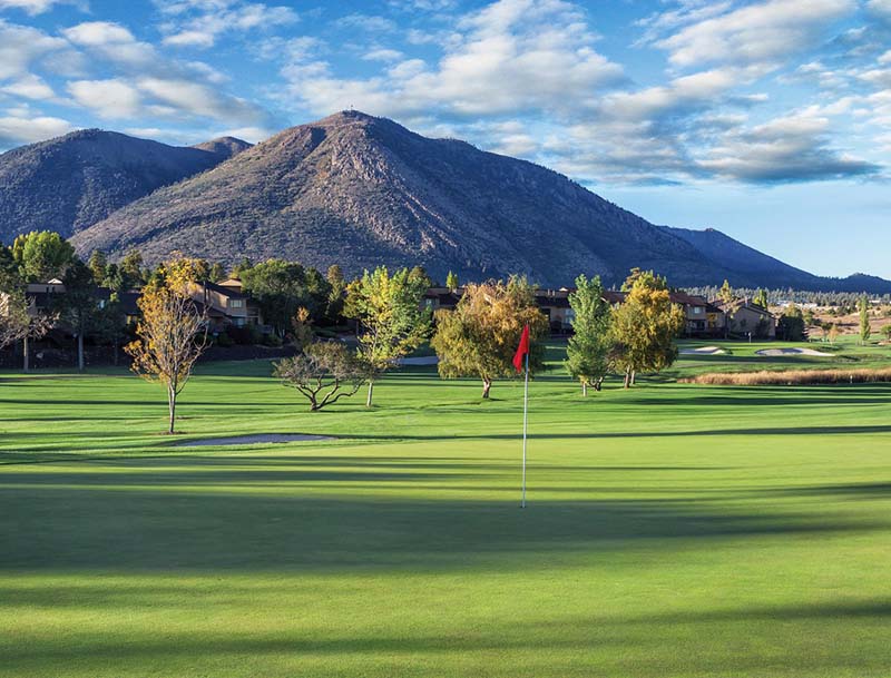 A panoramic view of the lush green golf course with towering mountains rising in the background.