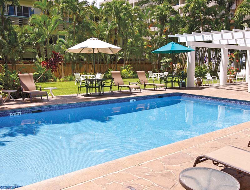 A tranquil pool with lounge chairs and umbrellas against the backdrop of lush tropical landscaping.