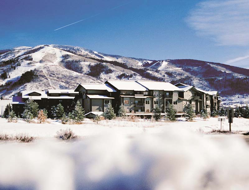 A sun-basked view of the resort amidst a snowy landscape, with the Rocky Mountains visible in the background.