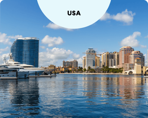 The West Palm Beach skyline overlooking a blue waterfront with luxury yachts docked in the harbor under a bright, partly cloudy sky.