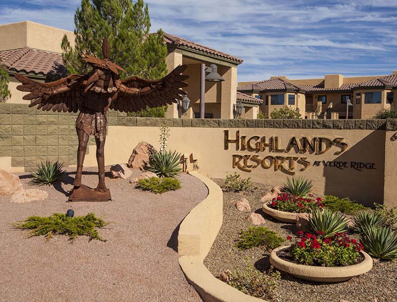 The entrance sign at Highlands Resort featuring a large metal sculpture and desert landscaping, with the sun-basked resort buildings visible in the background.