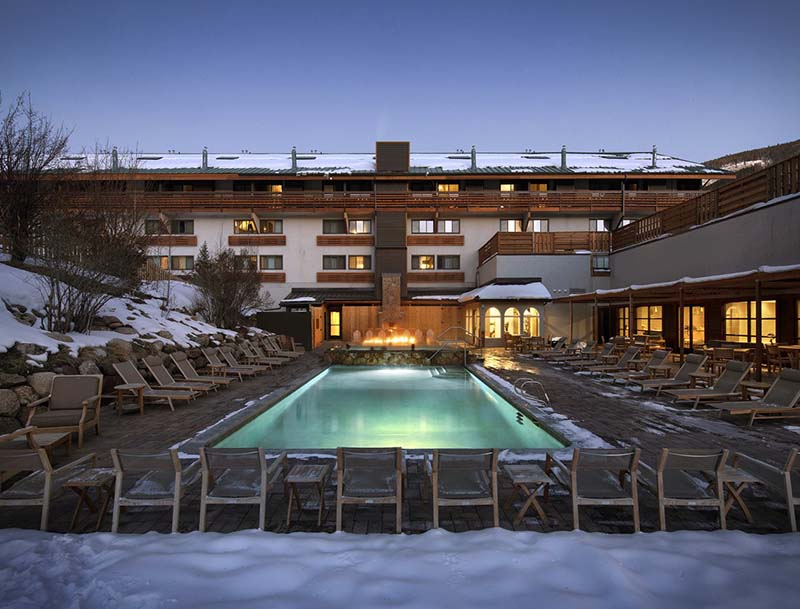 A view of the illuminated pool with fresh snow covering the surrounding deck area and resort rooftops.