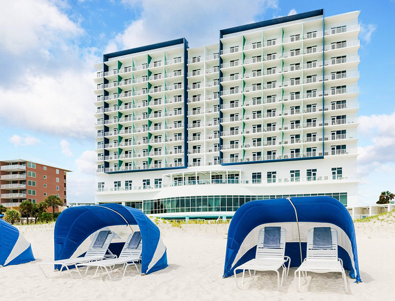 The resort’s bright white hotel tower as seen from the sandy beach lined with blue-and-white sun canopies and lounge chairs.