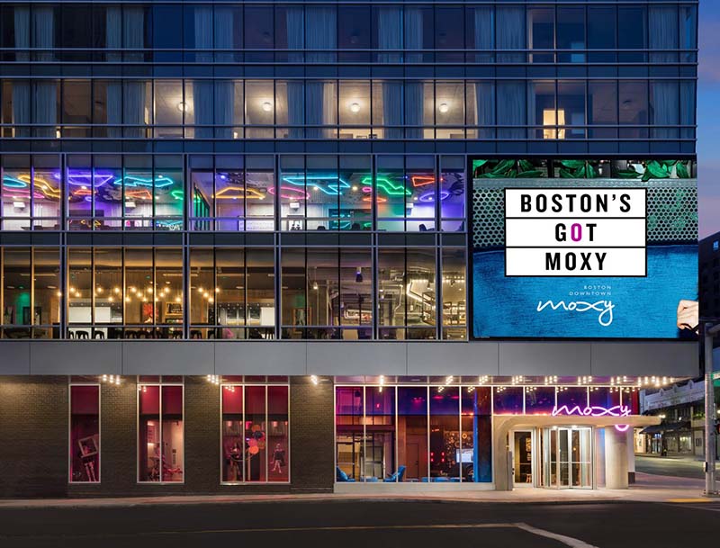 The hotel's elegant lobby and common areas basked in colorful lighting, as seen through the modern glass facade at dusk.