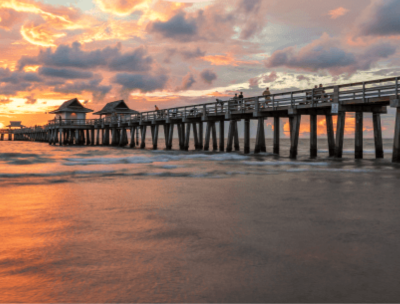 The Naples Pier extending into the ocean under a dramatic, orange and purple sunset.