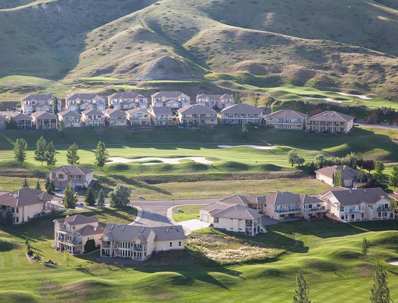 Aerial view of the resort buildings situated on a lush green golf course, with a mountain rising in the background.