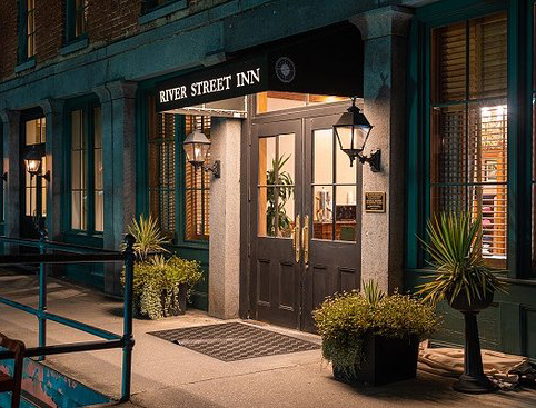 River Street Inn’s illuminated entrance at night, adorned with a black awning and potted greenery.