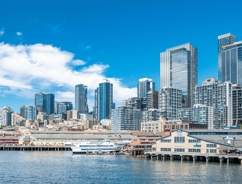 Bright daytime view of the San Diego, California waterfront and city skyline, featuring Pier 54 and a ferry boat docked in the harbor.
