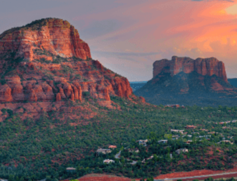 A scenic view of the red rock formations in Sedona, Arizona, towering over a lush, green valley.