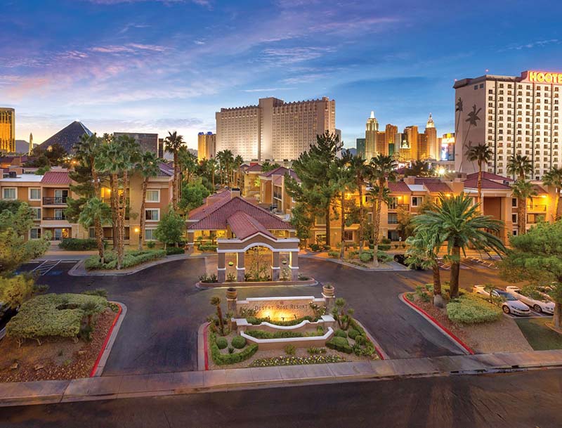 An aerial view showcasing the illuminated resort at dusk with the Las Vegas skyline visible in the distance.